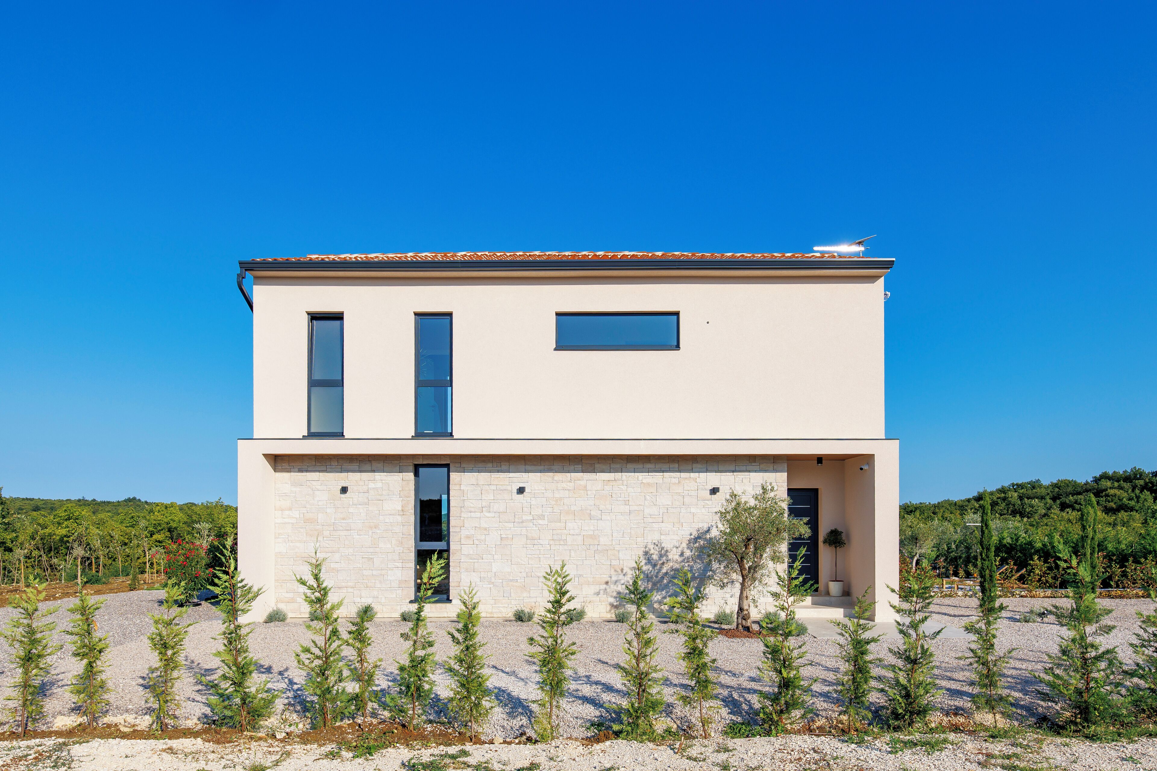A modern two-story building with a flat roof, a small balcony, and a gravel driveway.