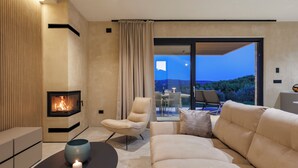 Un salon moderne avec une cheminée, un canapé, un fauteuil et une vue sur l’extérieur.