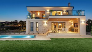 Une maison moderne à deux étages, dotée d’une piscine, d’un espace extérieur aménagé et d’un intérieur bien éclairé.