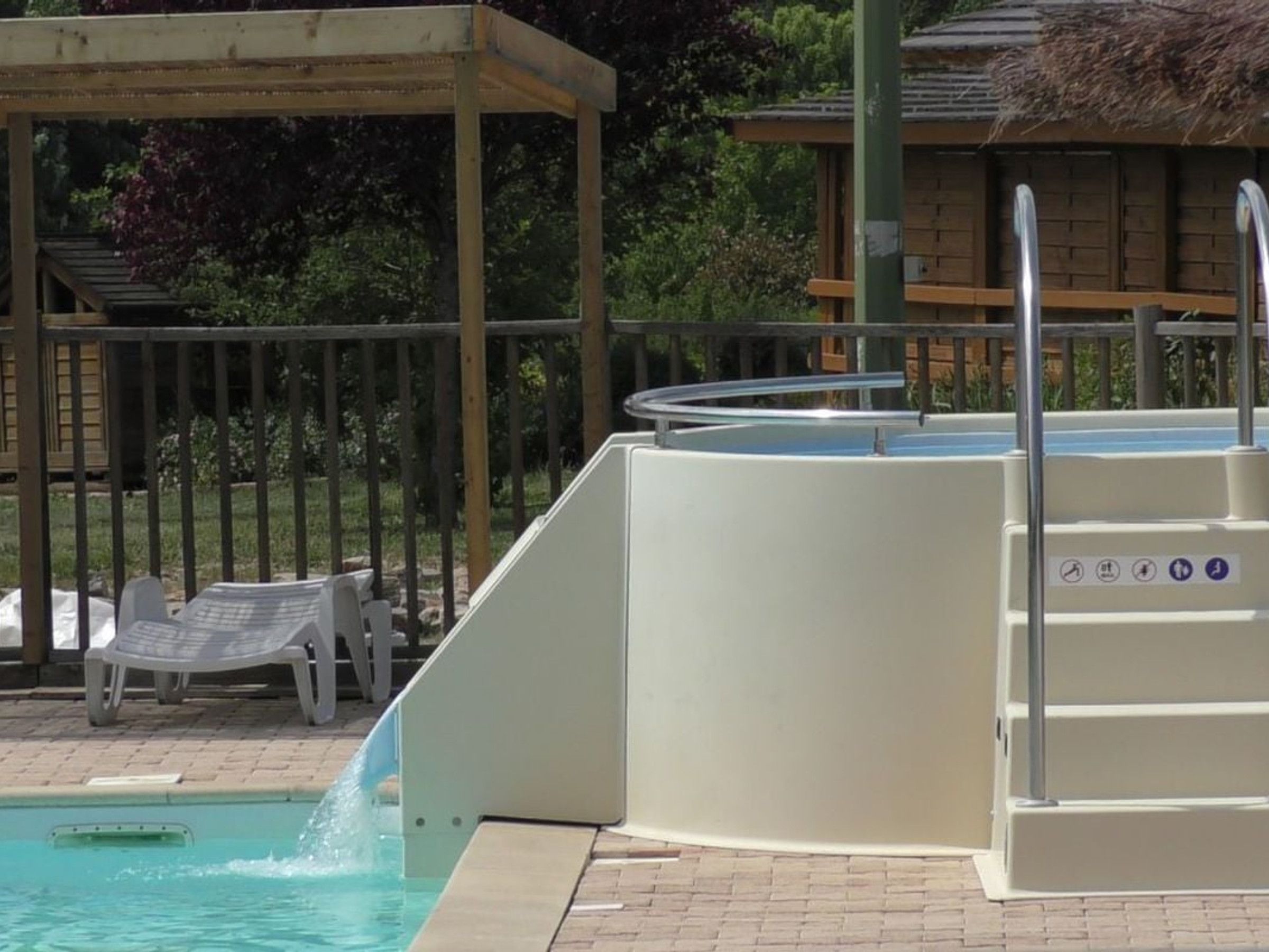 A swimming pool with a water slide, a covered seating area, and a lifeguard stand.