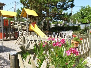 A playground with slides and climbing structures, surrounded by a wooden fence and potted plants. - Cozy chalet with terrace for 6 people (Darbres)