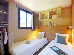 A hotel room with two beds, a wardrobe, a window, and a shelf with toiletries.