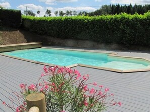 A rectangular swimming pool with a wooden deck surrounding it, bordered by green hedges. - Mobile Home with Terrace in Guégon (Guégon)
