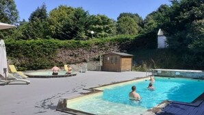 A swimming pool area with a wooden deck, a small wooden building, and lush greenery in the background.