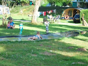 A grassy area with a water slide, tents, and a car parked nearby.