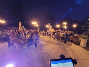 An outdoor dining area with tables and chairs, illuminated by overhead lights.