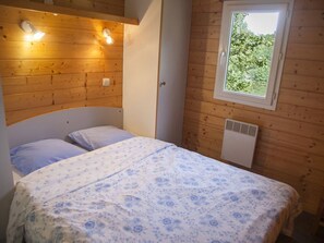 A single bed with a floral bedspread in a cabin-style room with wooden walls and a window.