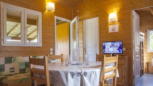 A wooden cabin interior with a dining table, chairs, a television, and a bench. - Spacious chalet for 8 people - Pond view - Terrace (Naucelle)