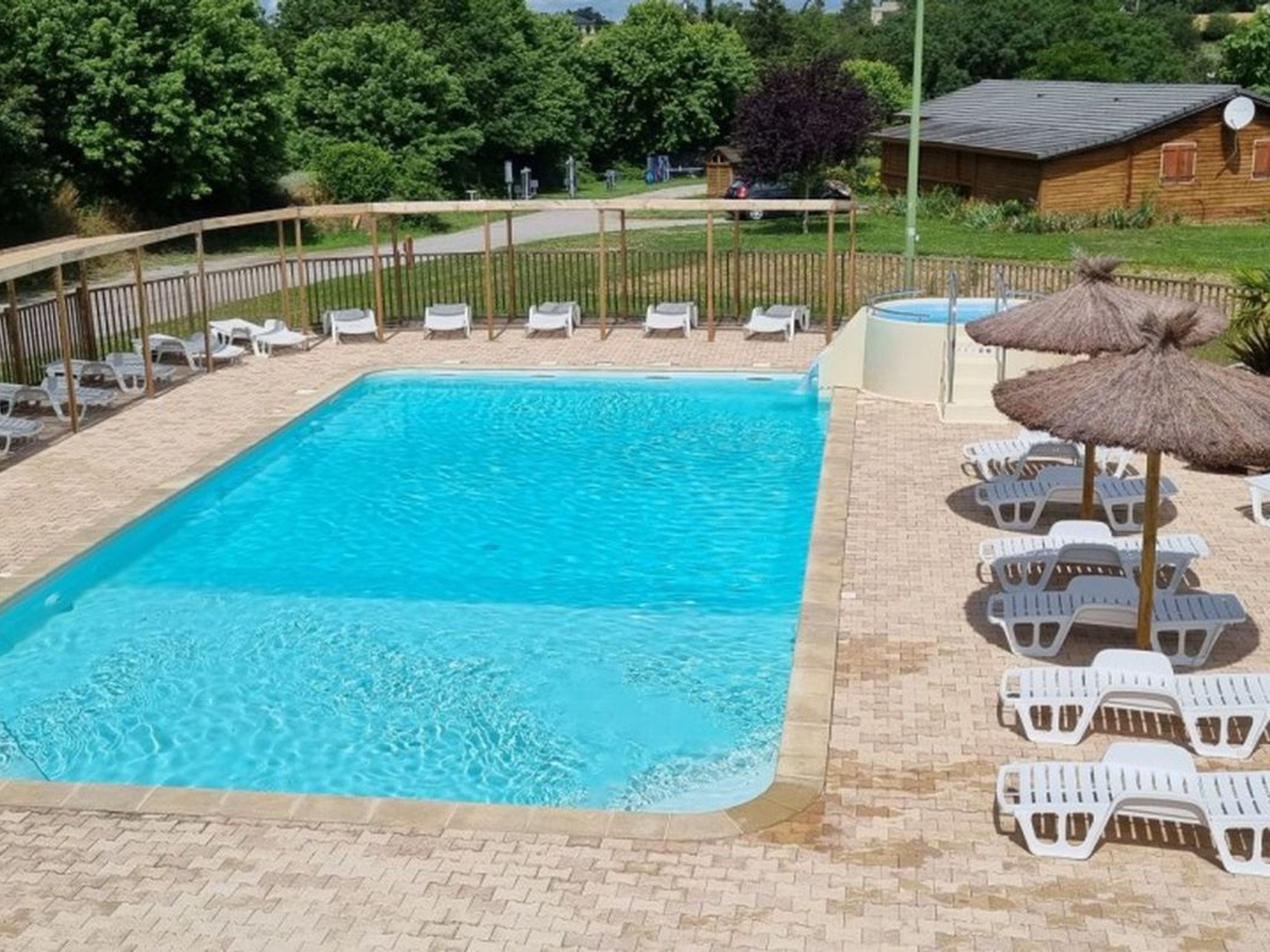 A rectangular swimming pool with a tiled deck, surrounded by white lounge chairs and thatched umbrellas.