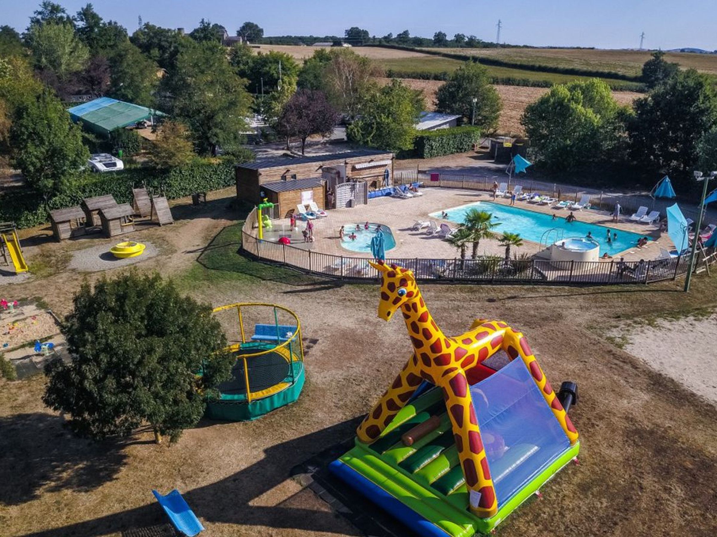 A fenced outdoor area with a pool, inflatable play structures, and a slide.