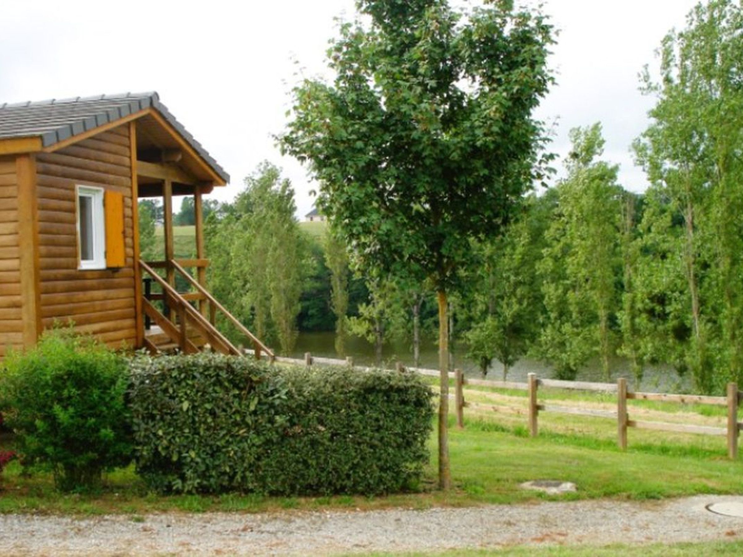 A wooden cabin with a porch and a staircase, surrounded by greenery and a body of water.