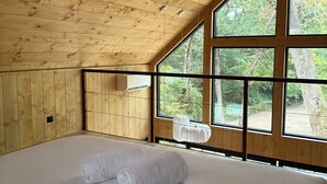 Une chambre dans un chalet en bois, avec un grand lit, des murs en bois et une fenêtre donnant sur une forêt.