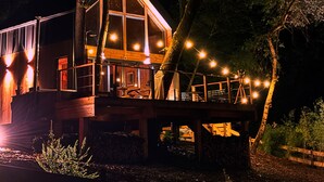 Une maison moderne dotée de grandes fenêtres, d’une terrasse et de guirlandes lumineuses.