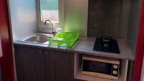Une cuisine compacte comprenant un évier, un égouttoir vert, une cuisinière et un four à micro-ondes.