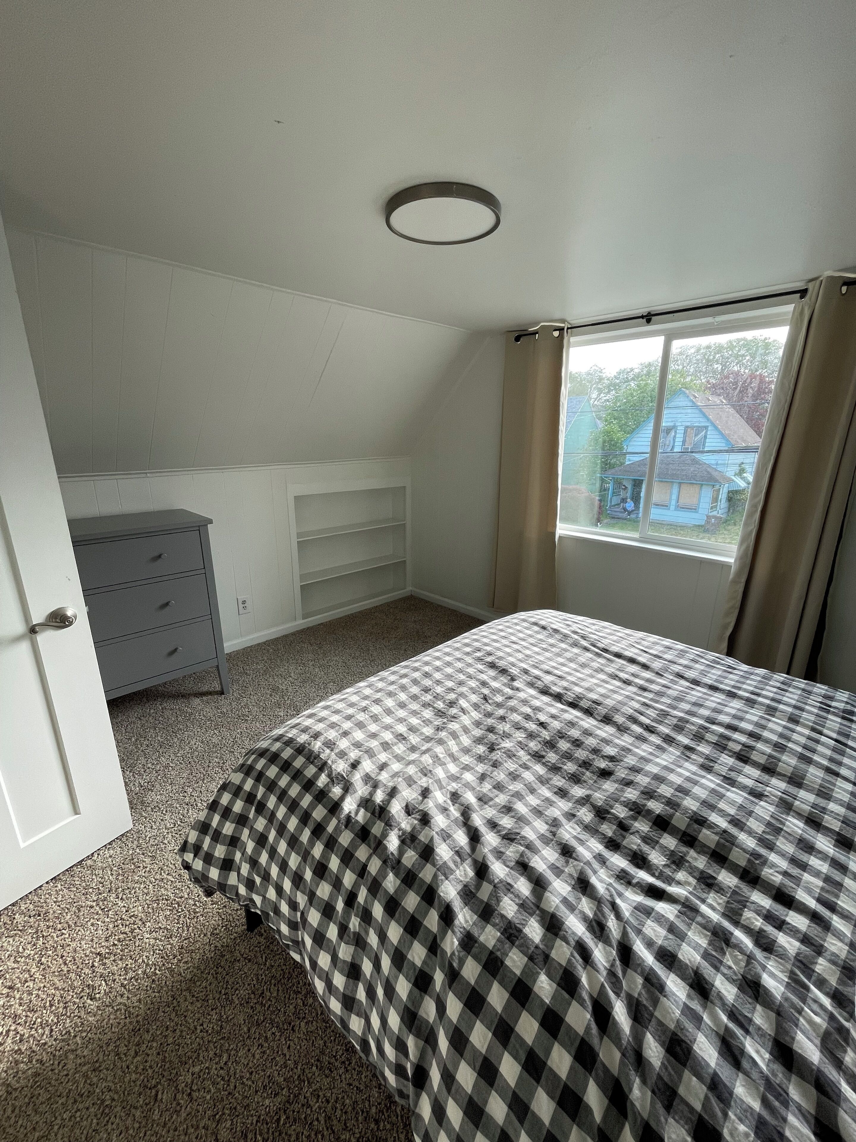 Een slaapkamer met een bed, een dressoir, een raam en een plafondlamp.