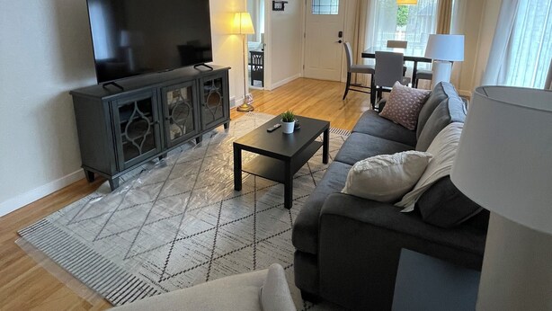 A living room with a flat-screen TV, dark wood furniture, a patterned rug, and a sofa with cushions.