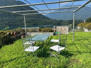 A glass table and chairs under a metal pergola, overlooking a lake with mountains in the background. - Mergozzo Beach Villa Panorama (Mergozzo)