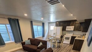 A modern living room with a brown sofa, a dining table with chairs, and a kitchen area with a microwave and oven. - Modern 1BR by Silicon Slopes – Workspace & 65” TV (American Fork)