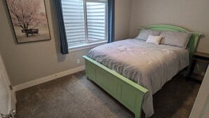 A bedroom with a green bed frame, a large window with blinds, a ceiling light, and a wall-mounted picture. - Modern 1BR by Silicon Slopes – Workspace & 65” TV (American Fork)