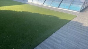 Zwembad met glazen omheining, omgeven door een houten terras en een gazon.