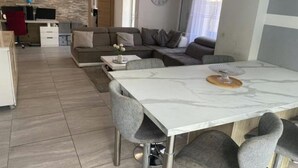 Een moderne woonkamer met een marmeren eettafel, grijs gestoffeerde stoelen, een grijze zithoek en een klok aan de muur.