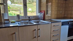 A kitchen with two sinks, wooden cabinets, a stove, and a window with a view of greenery.