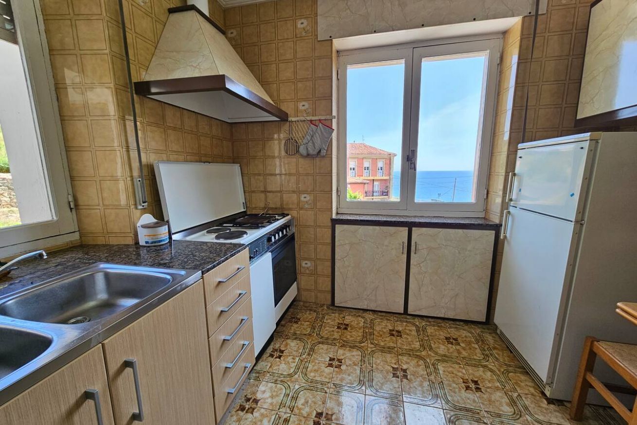A compact kitchen with a stove, sink, and window overlooking a building.