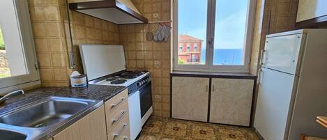 Uma cozinha compacta com fogão, pia e janela com vista para um prédio.