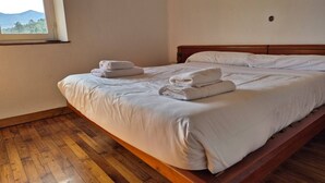 A single bed with white linens and a wooden headboard, a window with a view of greenery, and a wooden floor.