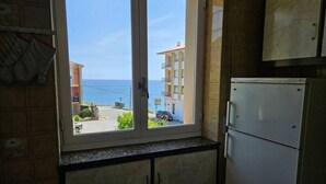 A kitchen with a view of the sea, a refrigerator, and cabinets.