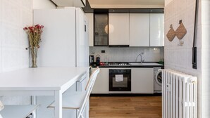 Una cocina moderna con armarios blancos, horno empotrado, lavadora y radiador.