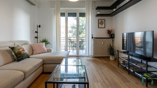 Una sala moderna con sofá, una mesa de centro de vidrio, televisor y balcón con vistas.
