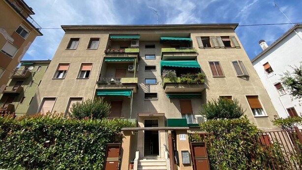 A multi-story residential building with balconies, a green awning, and a visible door number.