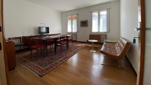 A spacious living room with a wooden floor, a dining area with a table and chairs, a sofa, and a television.