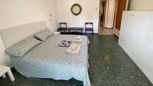 A bedroom with a large bed, two chairs, a small table, a mirror, and a wardrobe.