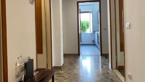 A hallway with a bench, a security camera, and a door leading to a balcony with a view of greenery.