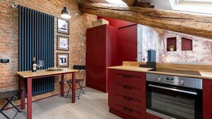A kitchen with exposed brick walls, a wooden table, red cabinetry, and a skylight. - La Dolce Suite | Porta Romana Metro (Milano)