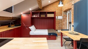 A compact kitchen with red cabinetry, a wooden dining table, and a loft bed with storage shelves. - La Dolce Suite | Porta Romana Metro (Milano)