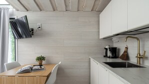 A modern kitchen with a wooden table, a white chair, a small potted plant, and a black coffee maker. - Koskisviitti 1 (Laukaa)