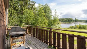 A wooden deck with a grill, overlooking a river and forested area. - Koskisviitti 1 (Laukaa)