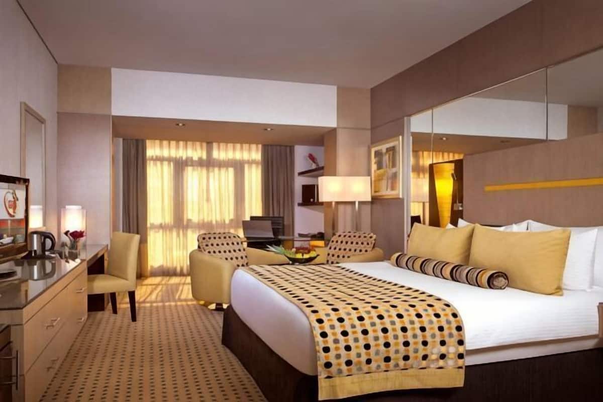A hotel room with a large bed, a desk, a chair, a TV, and a window with curtains.