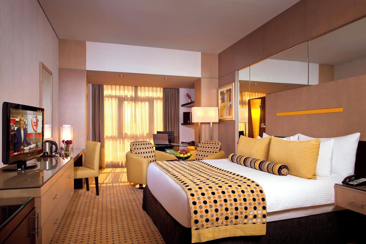 A hotel room with a bed, a desk with a computer, a TV, and a seating area with chairs.