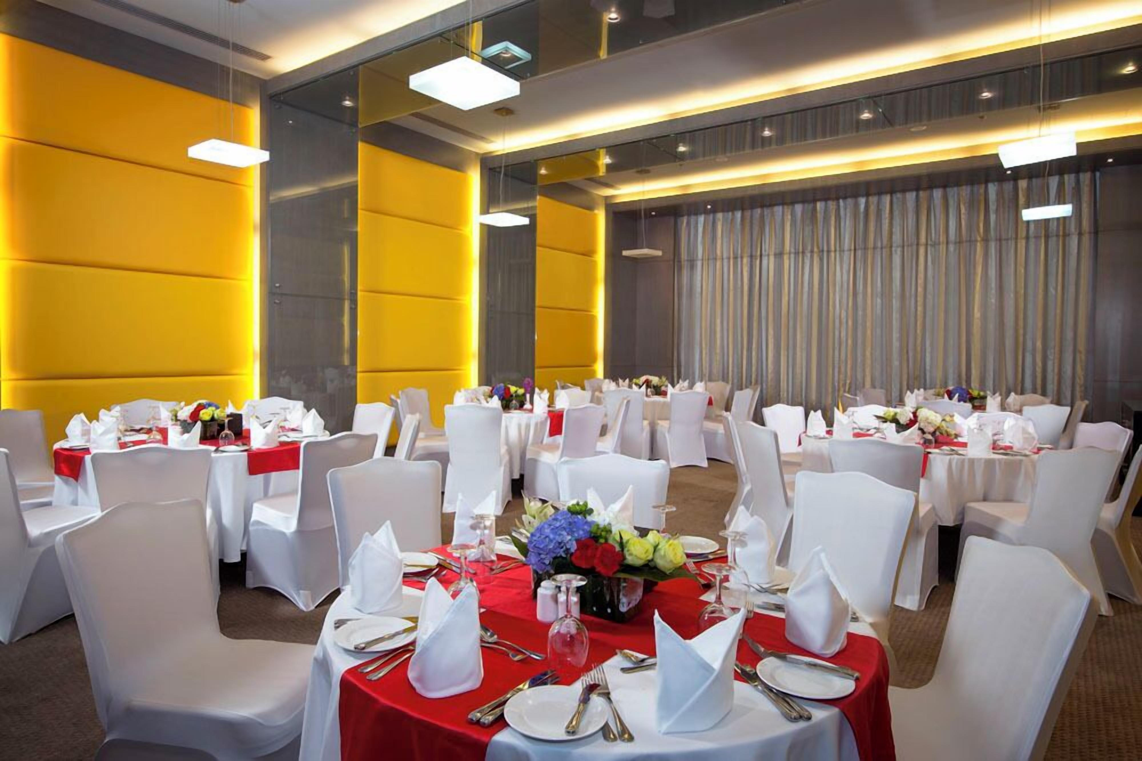 A banquet hall with round tables set for dining, white chairs, and red tablecloths.