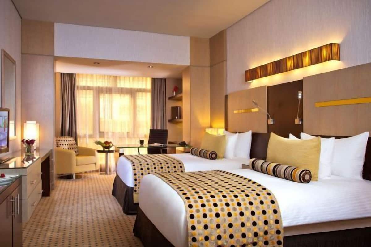 A hotel room with two beds, a desk, a chair, and a TV.