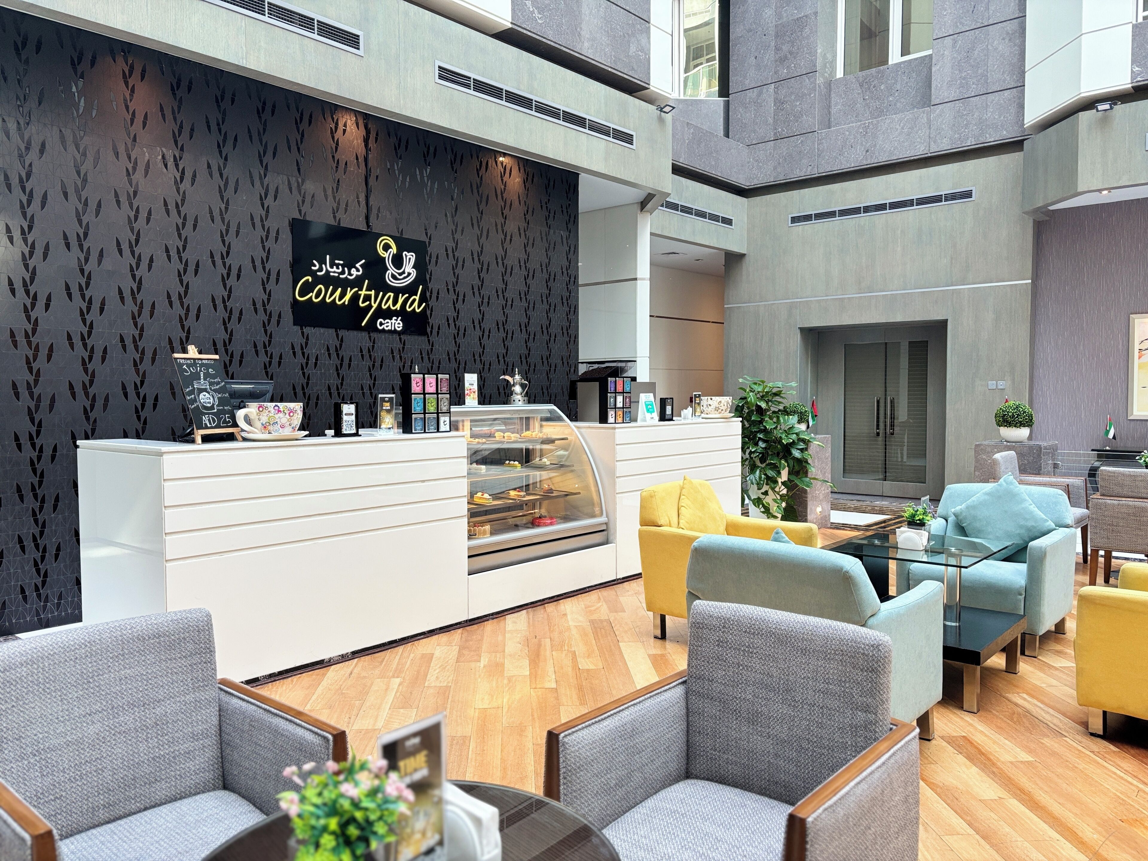 Ein modernes Café mit schwarzer Wand mit Blattmuster, einer Theke mit Glastreue und einer Sitzgelegenheit mit Stühlen und Sofas.