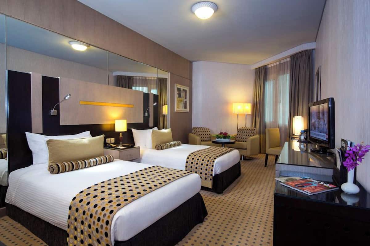 A hotel room with two beds, a TV, a desk, and a mirror.