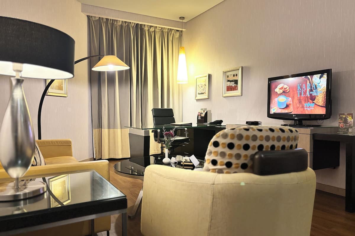 A hotel room with a dining table, a sofa, a television, and a desk with a computer.