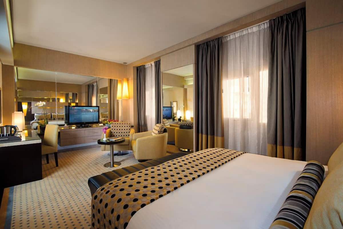 A hotel room with a bed, a desk, a television, a sofa, and a mirror.