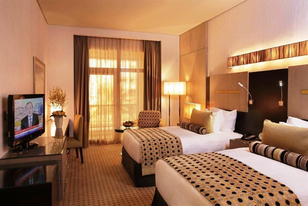 A hotel room with two beds, a desk with a TV, a chair, and a large window with curtains.