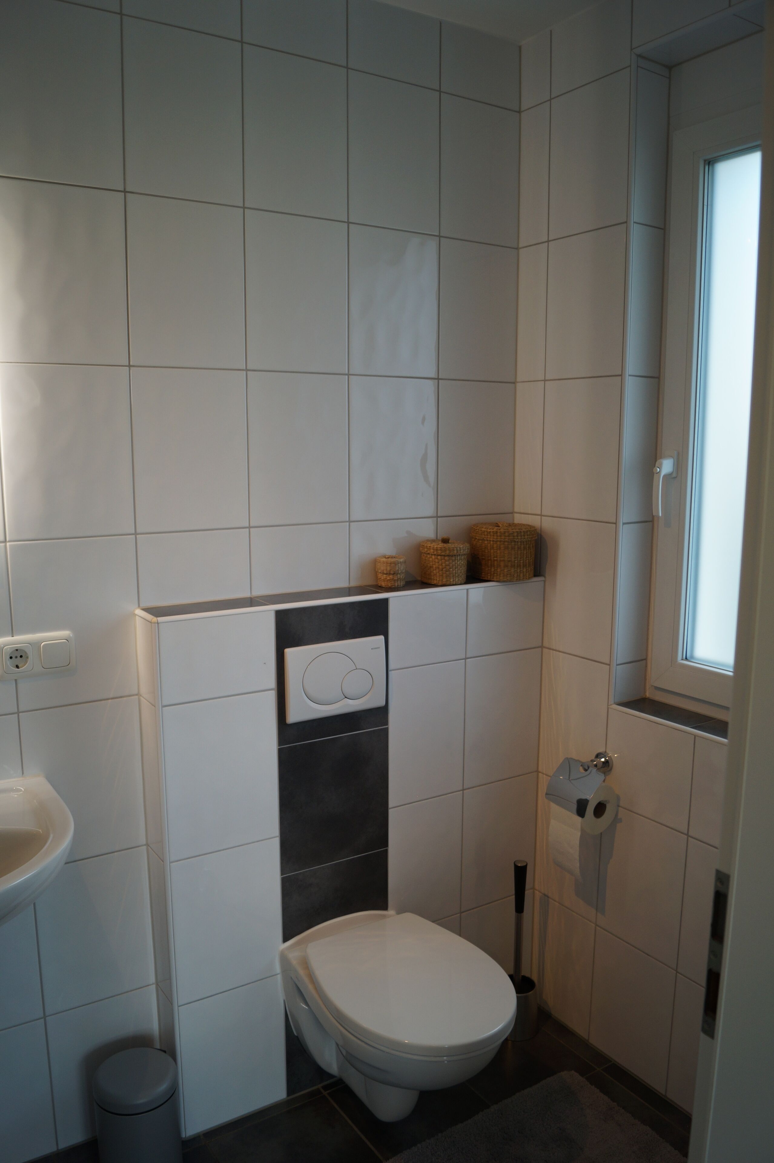 Ein kleines, sauberes Badezimmer mit Toilette, Waschbecken und Fenster.